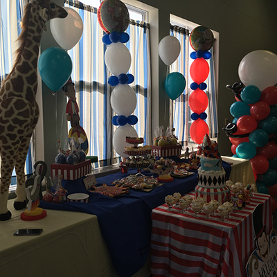 Birthday party dessert table with cake, cupcakes, and colorful balloons; a giraffe statue stands nearby.